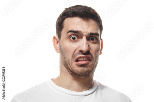 Closeup headshot of young Caucasian guy isolated on white background wearing white blank T-shirt showing strong emotion of disgust as if having smelled something stinky or met something unpleasant
