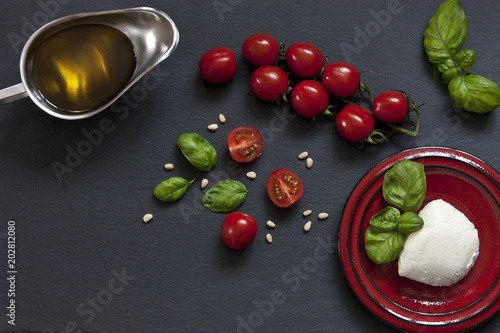 Close-up of red cherry tomatoes with white mozzarella cheese, olive oil and green leaves of basil on black background. Close-up, selective focus, shallow depth of field