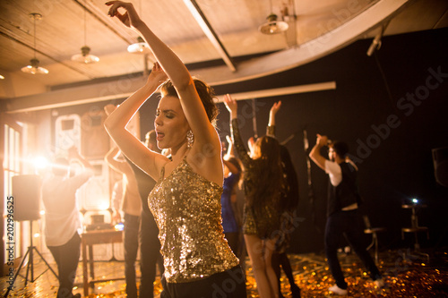 Crowd of trendy young people having fun in raving nightclub party, focus on pretty beautiful girl dancing on dance floor