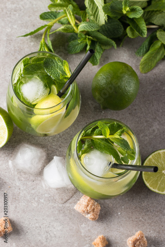 Fresh made mojito cocktail with lime, brown sugar, ice cubes and mint on a grey stone background. Alcoholic drink and lemonade concept.