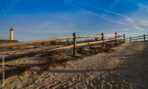 Wooden fence leads to beach near lighthouse in Cape May, NJ, on a sunny morning