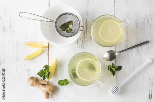Ginger tea with mint, lemon and honey in a glass cup on a white wooden table, top view