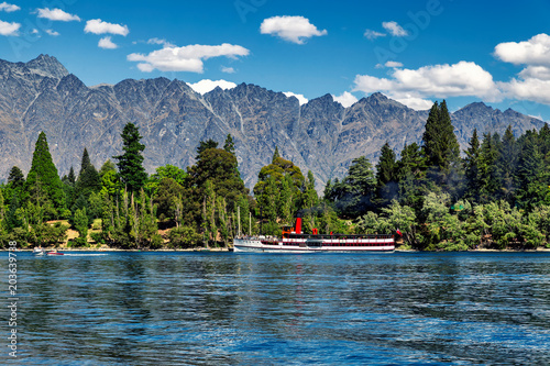 Steam-powered ship on lake Wakatipu surrounded by coniferous forest and mountains in Queenstown, New Zealand
