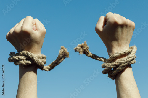 Hands tearing shackles the background of blue sky. Concept of freedom