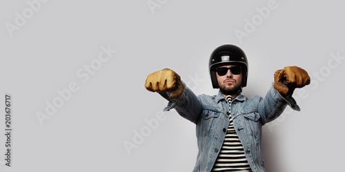 Young biker in a blue denim jacket pretending to ride a motorcycle isolated on white background. Horizontal. Wide