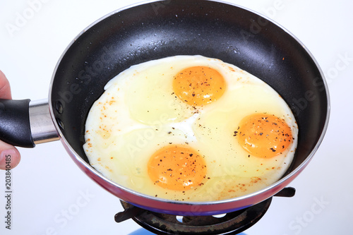 Jajko sadzone na teflonowej patelni posypane pieprzem nad kuchenką gazową.
