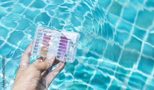Swimming pool check kit in girl hand dipping in clear water, summer outdoor day light, water quality test kit