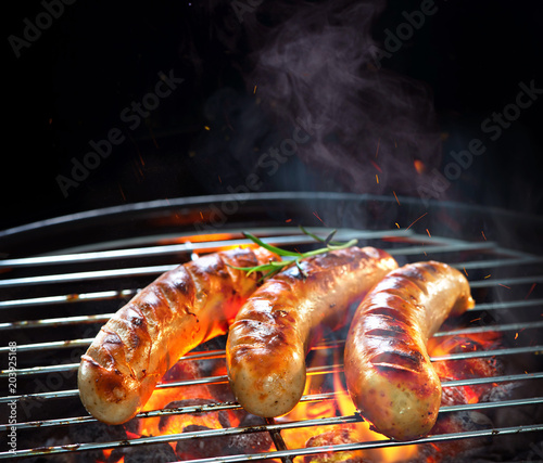 Grilled sausages on grill with smoke and flame