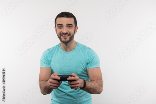 Interesting entertainment. Joyful bearded man holding a video game console while having fun at home