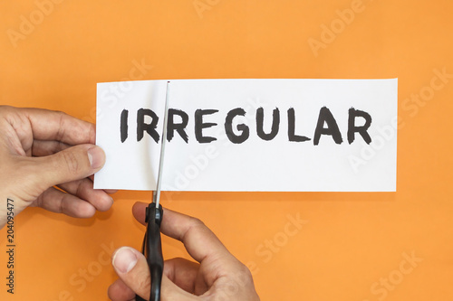 Closeup man cutting paper of irregular word. concept for self belief, positive attitude and motivation. irregular is regular concept.