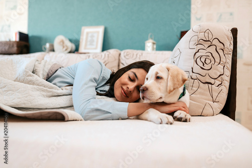 Attractive young girl with dog laying on a bed.
