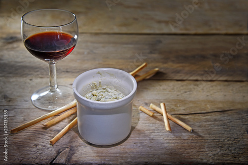 potted blue stilton cheese in a ceramic jar, port wine and some nibble sticks on a dark rustic wooden table, copy space