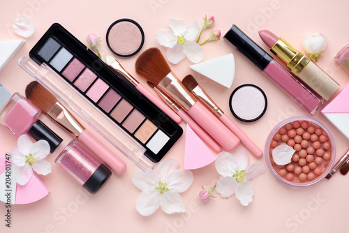 Makeup brush and decorative cosmetics with apple blossom on pink background. Top view