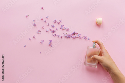 perfumery and floral scent concept. hand holding stylish bottle of perfume with spray of lilac flowers on pink background. creative trendy flat lay with space for text. modern image