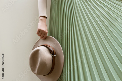 Hat, beige blouse and turqoise pleats skirt on light street backgraund. Fashion and stylish concept.