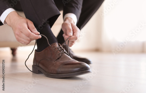 Man putting on elegant leather shoes indoors, closeup