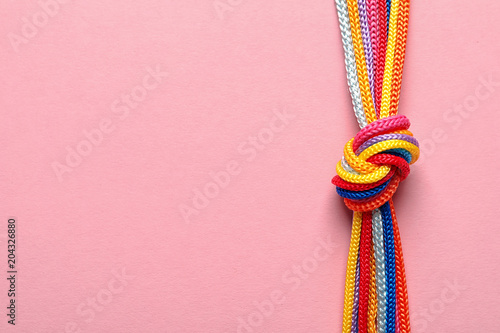 Different ropes tied together with knot on color background. Unity concept