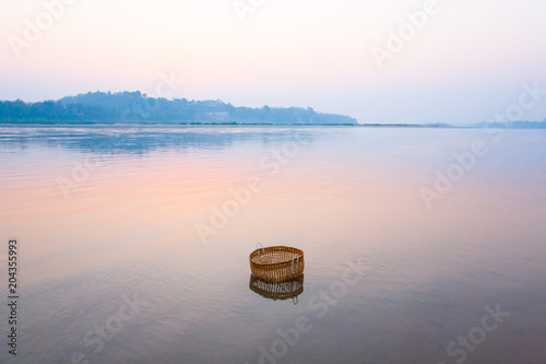 A bamboo basket is dips in mekong river at sunrise.