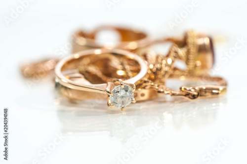 Real gold rings, chains, diamonds and gems on shiny surface, white background.