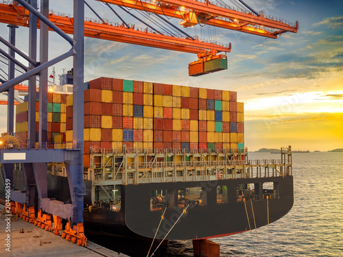 The container vessel during discharging at an industrial port and move containers to container yard by trucks.