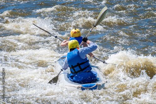 Rafting, kayaking. Two sportsmen in sports equipment are sailing on a rubber inflatable boat in a boiling water stream. Teamwork. Water splashes close-up. Extreme sport.