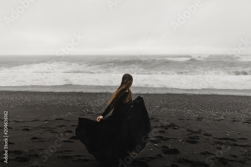 woman wearing a black dress on the black beach in iceland during a storm