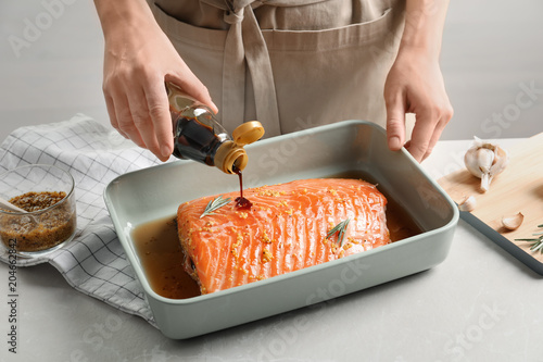 Woman pouring marinade onto raw salmon in baking dish, closeup