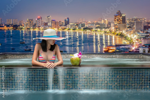 woman i8n bikini enjoy city light in background in swimming pool on rooftop of building, bay of pattaya city Thailand