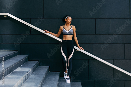 Woman in sportswear relaxing after workout, standing on staircase