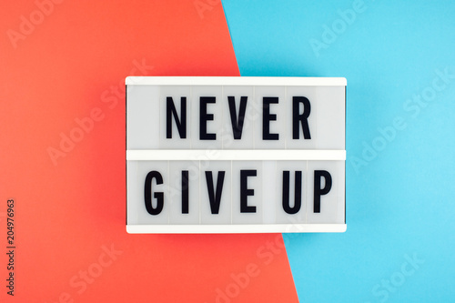 Never give up - text on a display lightbox on blue and red bright background.