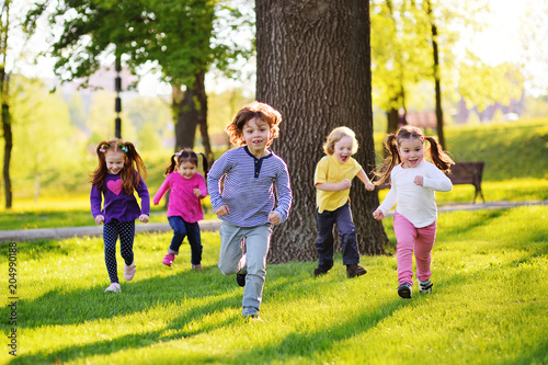 many young children smiling running along the grass in the park. Childhood, Children's Day, vacation, vacation, adventure, friendship.