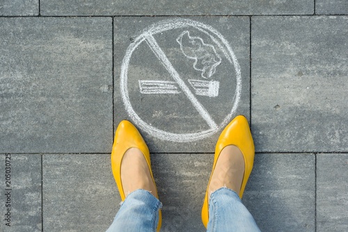 Female feet with picture no smoking painted on the grey sidewalk