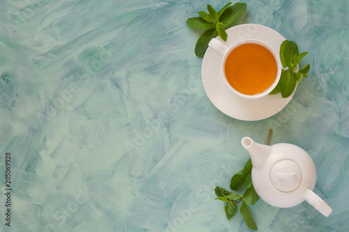 Tea concept. Teapot and cup with green herbal tea decorated mint leaves on wooden background. Top view. Copy space. Flat lay. Toned