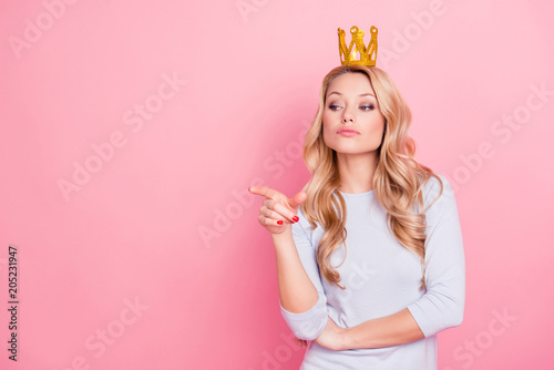 Portrait with copyspace empty place of confident proud arrogant woman with gold crown on her head pointing forefinger, miss I want, isolated on pink background