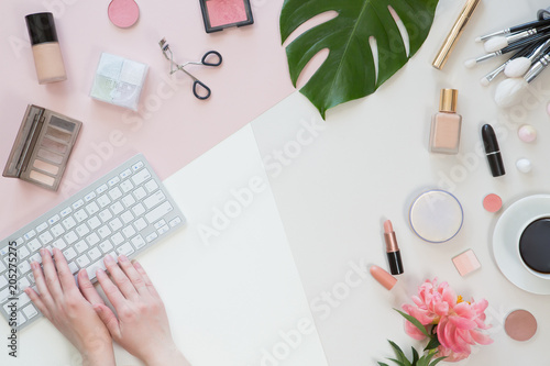 Flat lay, top view of pastel woman office table desk. Workspace with paintbrush, laptop, peony flowers, palm tropical leaves, cosmetics, diary on white and pink background. Online shopping concept
