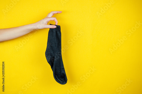 old smelly holey sock in hand on a yellow background