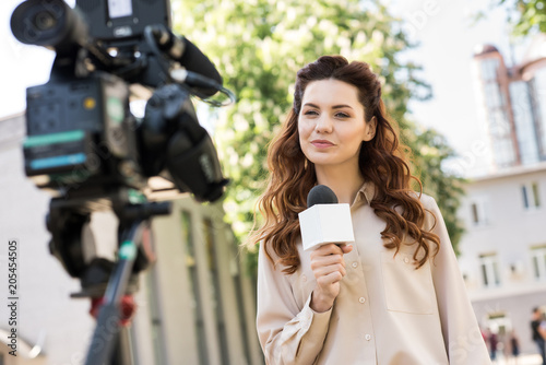 beautiful female journalist with microphone talking to digital video camera