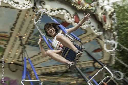 Closeup of exhilarated young girl riding very fast on an amusement park swinging carousel with main subject slightly out of focus to depict speed