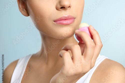 Young woman applying balm on her lips against color background, closeup