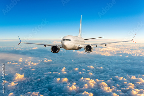 Front view of aircraft in flight. The passenger plane flies high above the clouds and blue sky. Business travel and summer trip concept