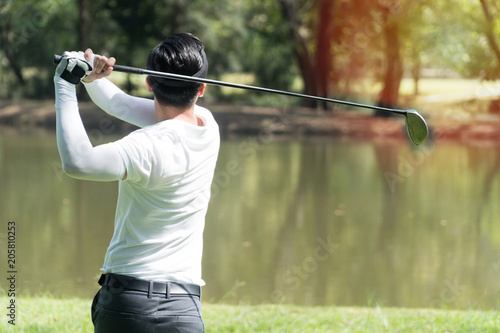The back of golf Player in white shirt swinging glof. Young man practicing his swing on the golf course.