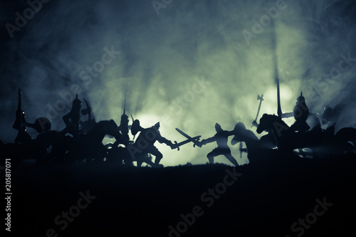 Medieval battle scene with cavalry and infantry. Silhouettes of figures as separate objects, fight between warriors on dark toned foggy background. Night scene.