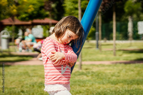 sad little girl stands next to a swing at the playground on a summer day