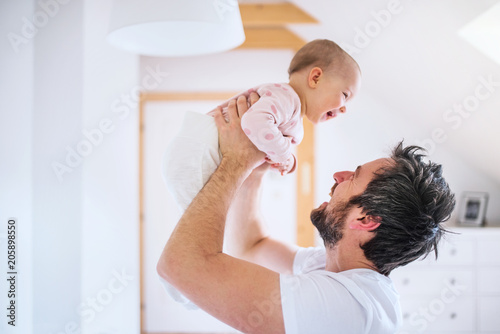 Father with a toddler girl in bedroom at home, having fun.