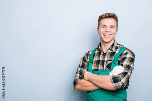 Portrait of kind cheerful excited smart professional friendly expert handsome with beaming shiny smile handyman wearing green overalls standing with folded hands isolated on gray background copyspace