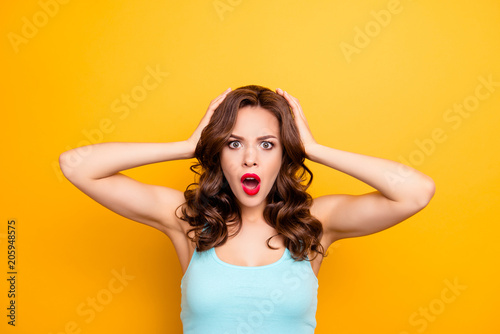 WTF! Portrait of irritated impressed woman holding two hands on head keeping wide open mouth looking at camera isolated on yellow background