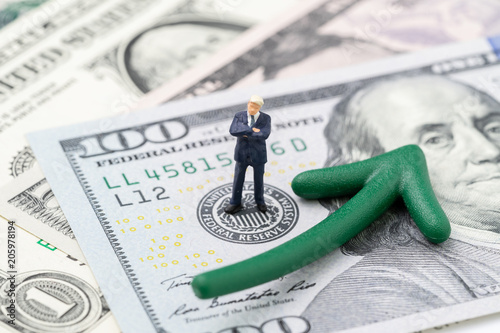 FED consider interest rate hike, world economics and inflation control, miniature businessman leader standing on US Federal Reserve emblem on dollars banknote with green arrow rising up