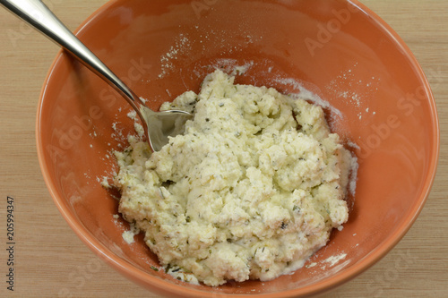 Close up of mixing herbs into ricotta cheese in orange bowl with spoon