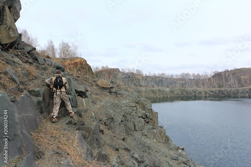 Man with a backpack walking along the steep bank of a flooded quarry, Toguchinsky district, Siberia, Russia