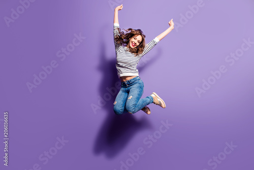 Portrait of cheerful positive girl jumping in the air with raised fists looking at camera isolated on violet background. Life people energy concept